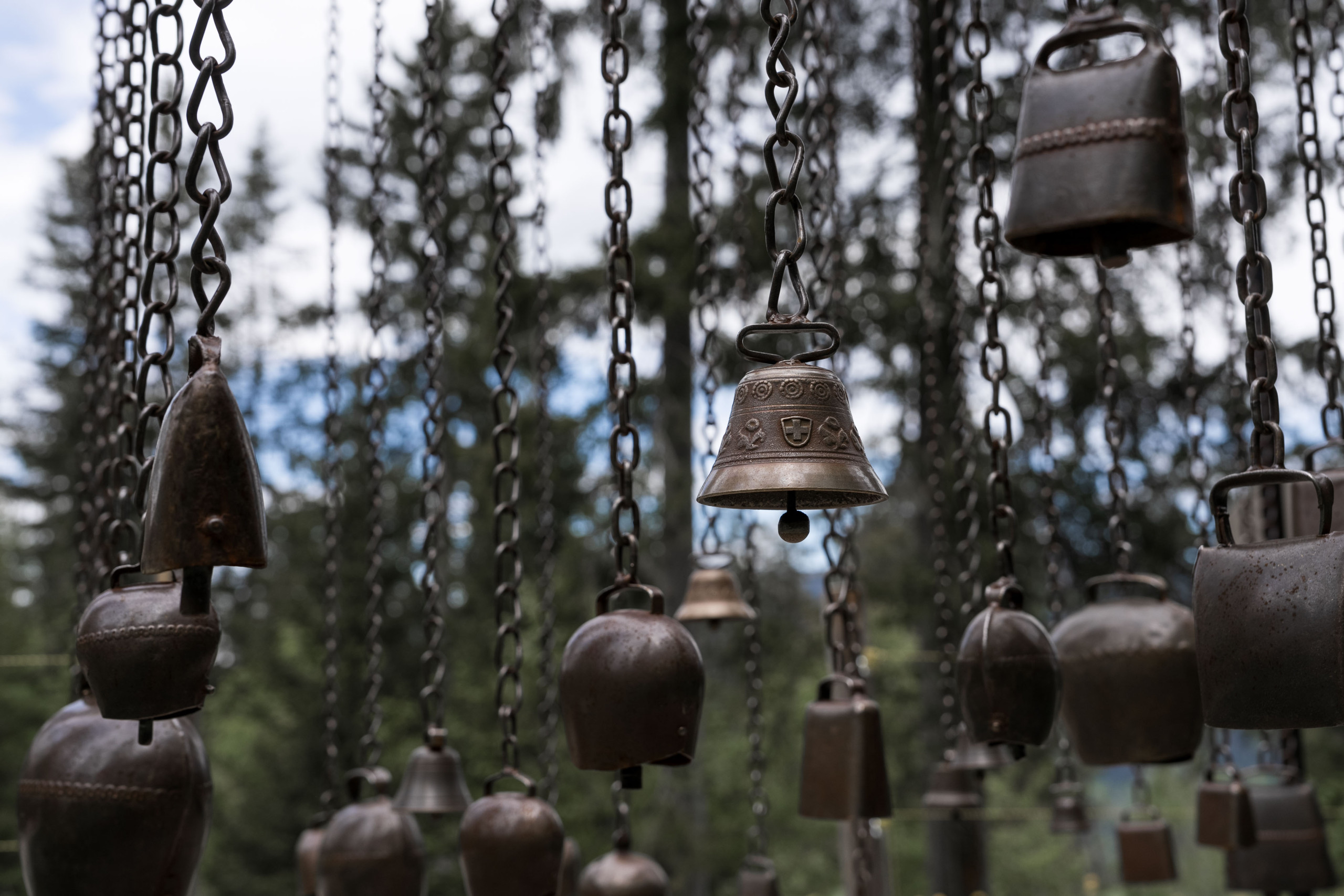 Unterschiedliche Schellen und Glocken hängen an Metallketten im Wald des Klangweg Toggenburg