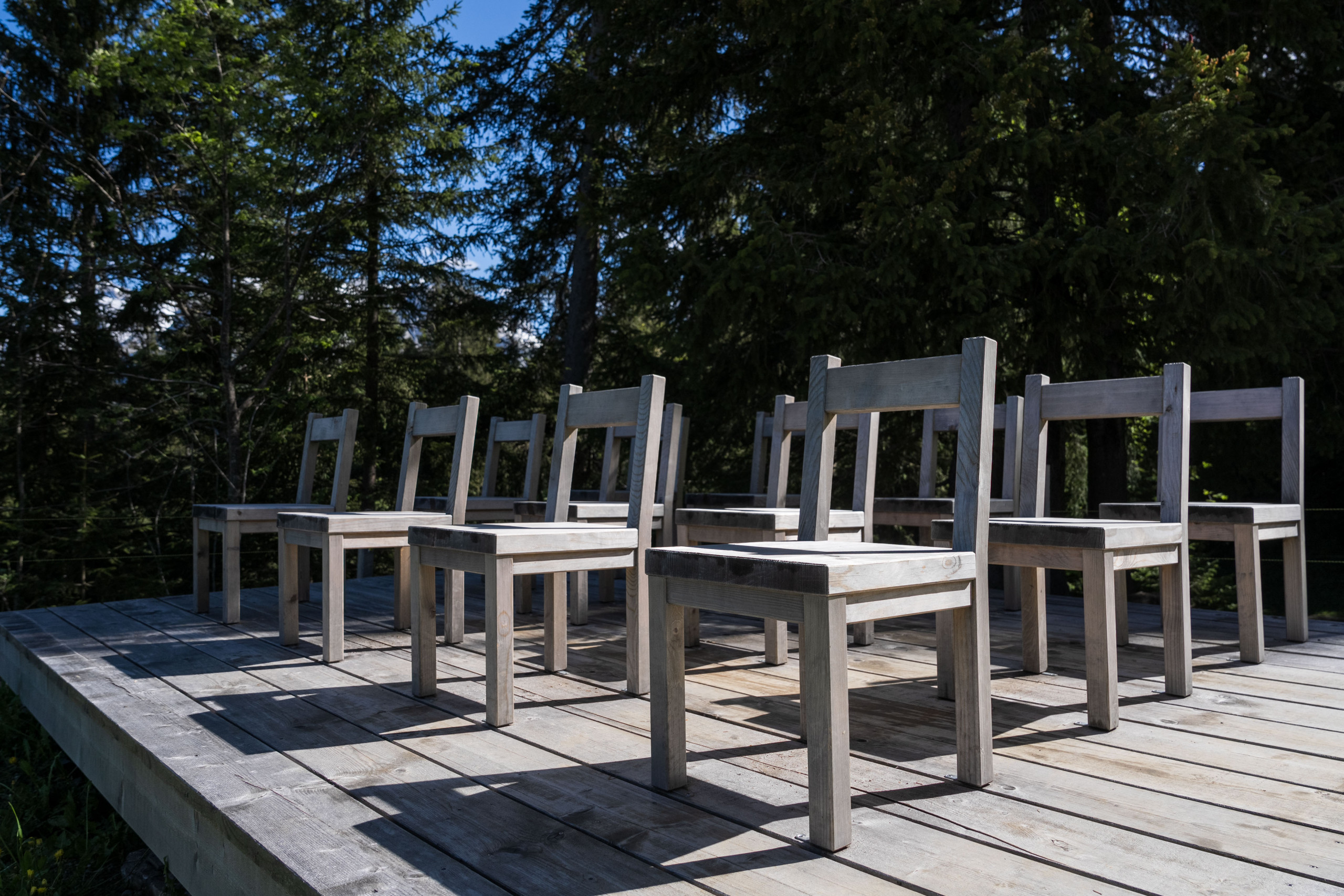 12 Holzstühle stehen auf einer Holzplattform mitten im Wald auf dem Klangweg Toggenburg